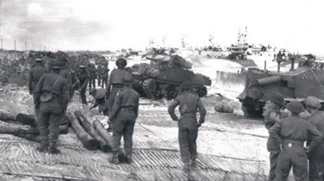 Des chars du 1st Hussars et des hommes de la 7e Brigade d’infanterie débarquent sur la plage encombrée à Courseulles-sur-Mer le 6 juin 1944. Photo par Ken Bell. Ministère de la Défense nationale / Archives nationales du Canada, PA-128791.